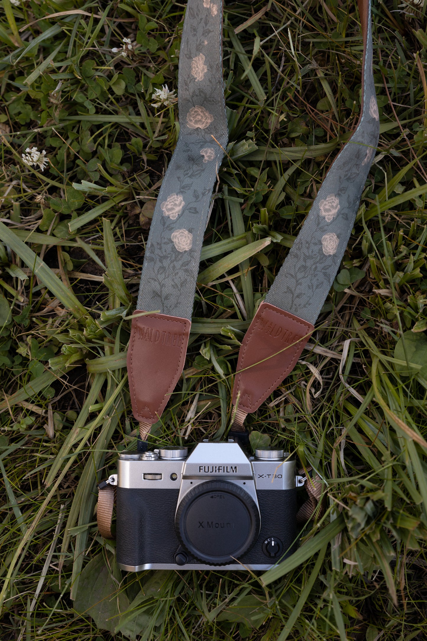 Vine camera strap laying on the grass vine with yellow flowers