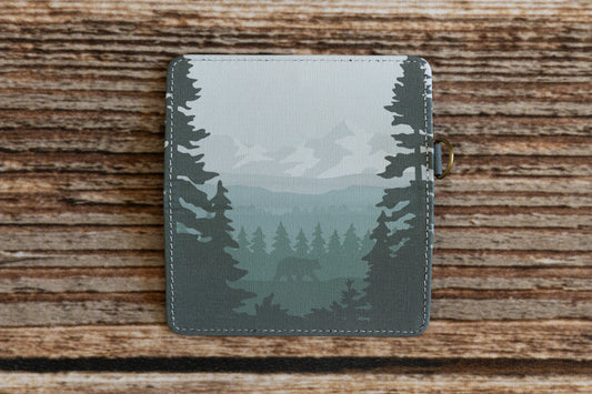 A opened green Wildtree Outdoor SD card holder featuring a forest and subtle bear design lies flat on a rustic wooden surface.