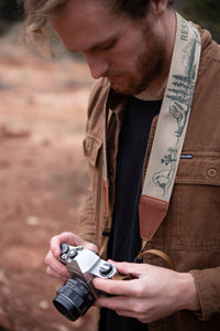 man looking at film camera with Wildtree national park camera strap around neck