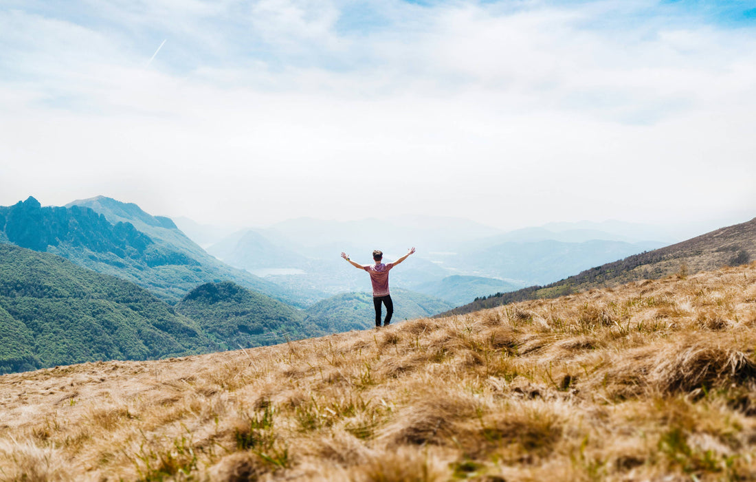 man with his arms up looking out across mountains and valley