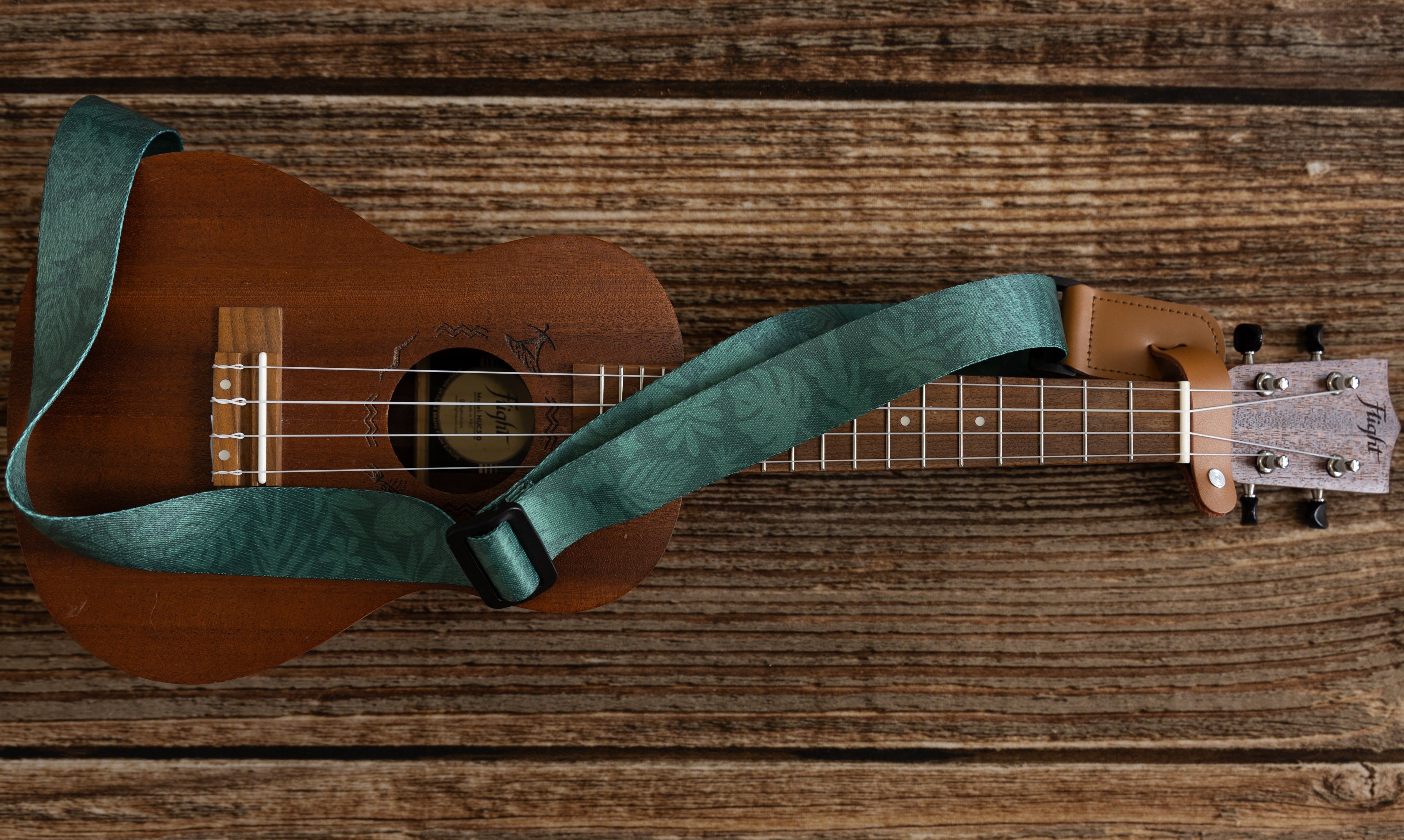 Green Tropical leaf printed ukulele strap connected to ukulele instrument lying on floor