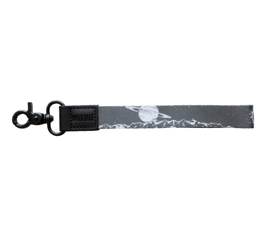 A gray wristlet keychain with a black and white design featuring mountains and a planet with rings, laid out straight on a plain white background.