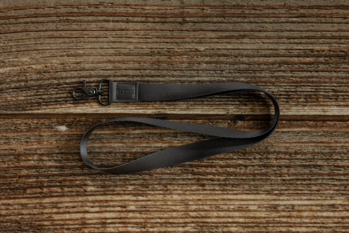Black Neck Lanyard coiled on a rustic wood surface, showing the full strap length