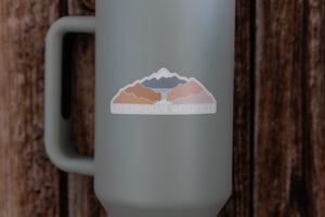 sticker design featuring colorful mountains and a waterfall with the words "Let's Go Chase Waterfalls" placed on Stanley Cup