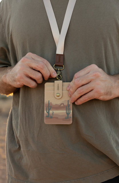 Close-up of a person holding the Desert ID badge holder, worn on a lanyard over an olive green shirt.