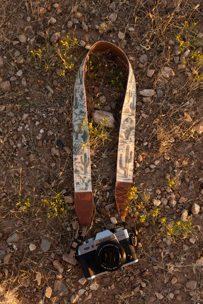 Western landscape camera strap lying on desert ground with desert flowers