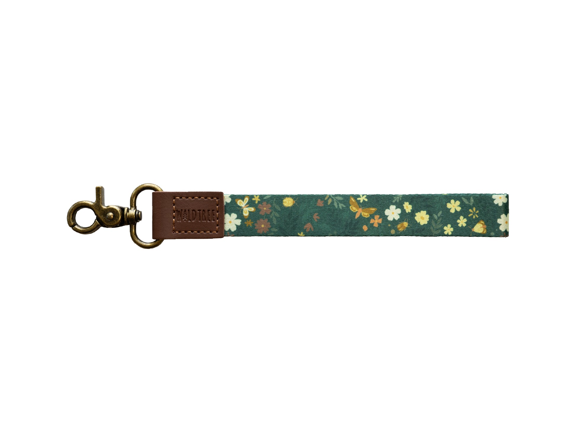 Flat lay of the Flutter & Fern wristlet keychain on a white background, showing the dark green strap printed with white daisies, small brown and yellow flowers, and gold butterflies, a brown vegan-leather tab embossed with the WILDTREE logo, and a bronze swivel clasp.