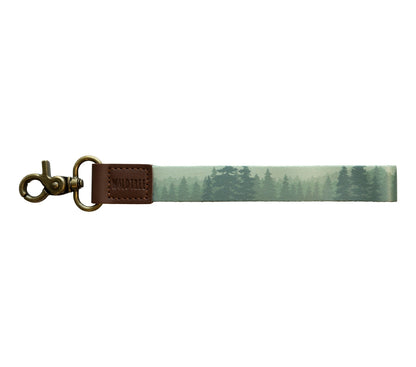 A product photo against a plain white background showing a wristlet keychain with a misty green forest print on a polyester strap.