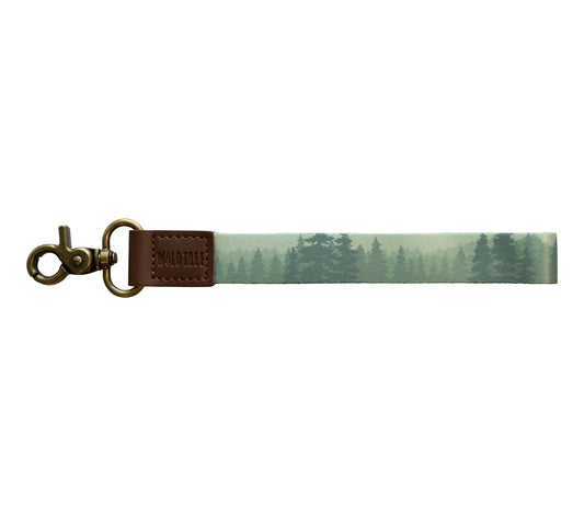 A product photo against a plain white background showing a wristlet keychain with a misty green forest print on a polyester strap.
