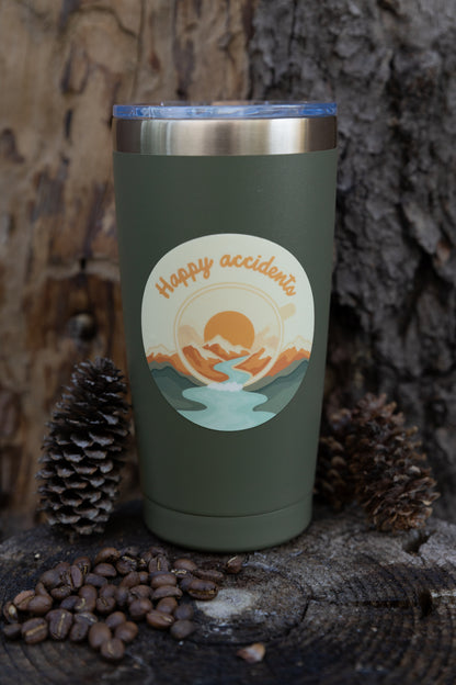 A top-down overhead perspective flat lay of the die-cut "Happy Accidents" sticker resting on a rustic wood tree stump. The sticker shows the campfire mug design with an abstract color burst, surrounded by dried pinecones, scattered roasted coffee beans, and a silver coffee maker.