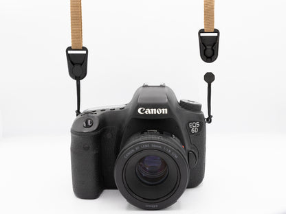Canon EOS 6D camera with a tan neck strap attached to both strap lugs using Wildtree low-profile quick-release buckle connectors, with a quick-link paracord pull hanging unattached from the right lug for comparison