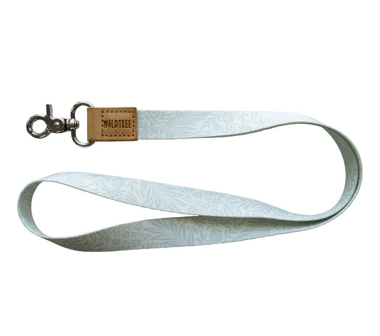 Flat lay of the Meadow Mist neck lanyard on a white background, showing the full pale sage-gray strap printed with a soft white fern leaf pattern.