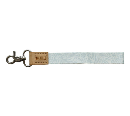 Flat lay of the Meadow Mist wristlet keychain on a white background, showing the pale sage fern-print strap.