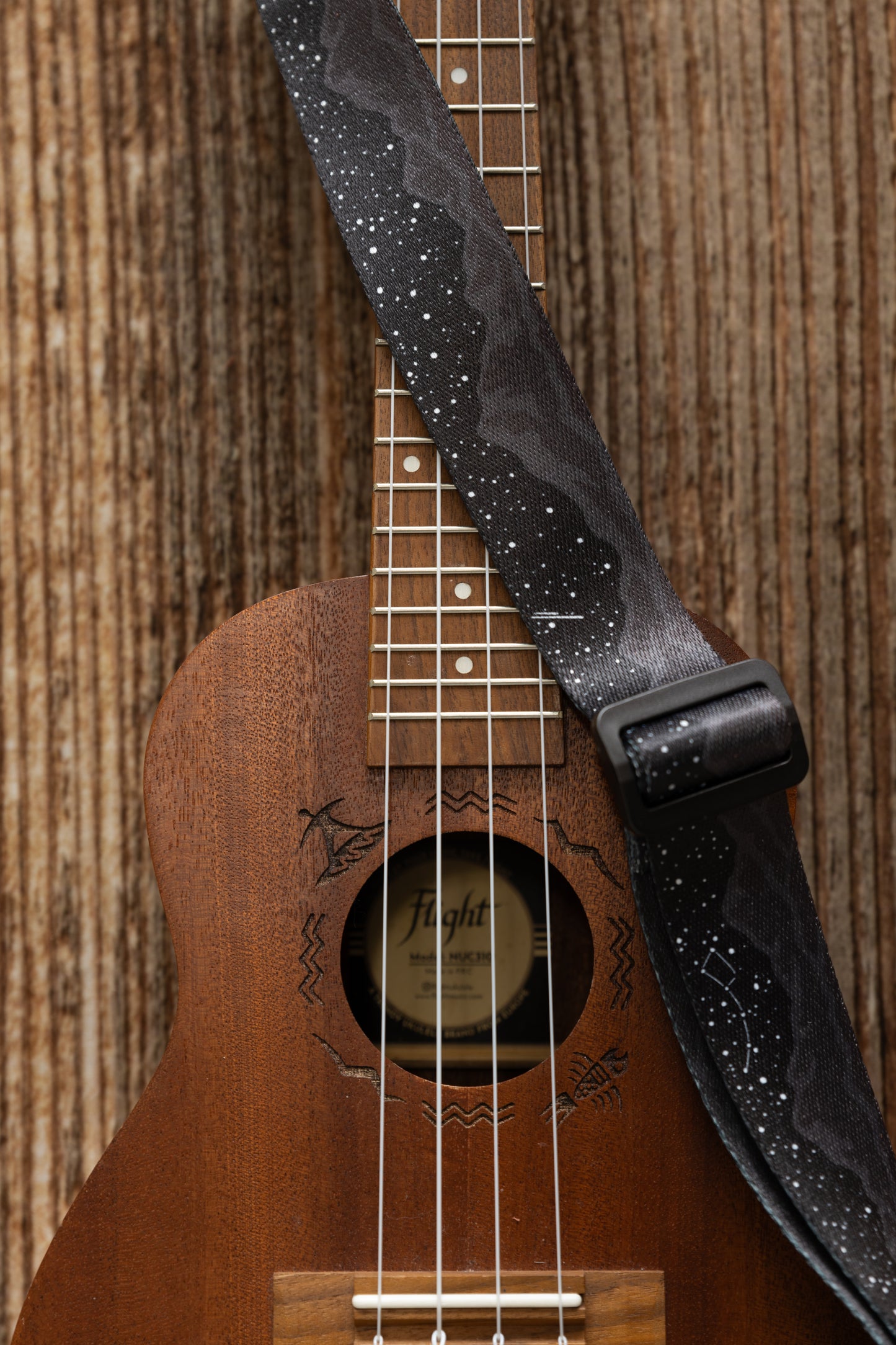 Black Ukulele Strap Strap Printed with Mountains and Stars lying across Ukulele on wood floor