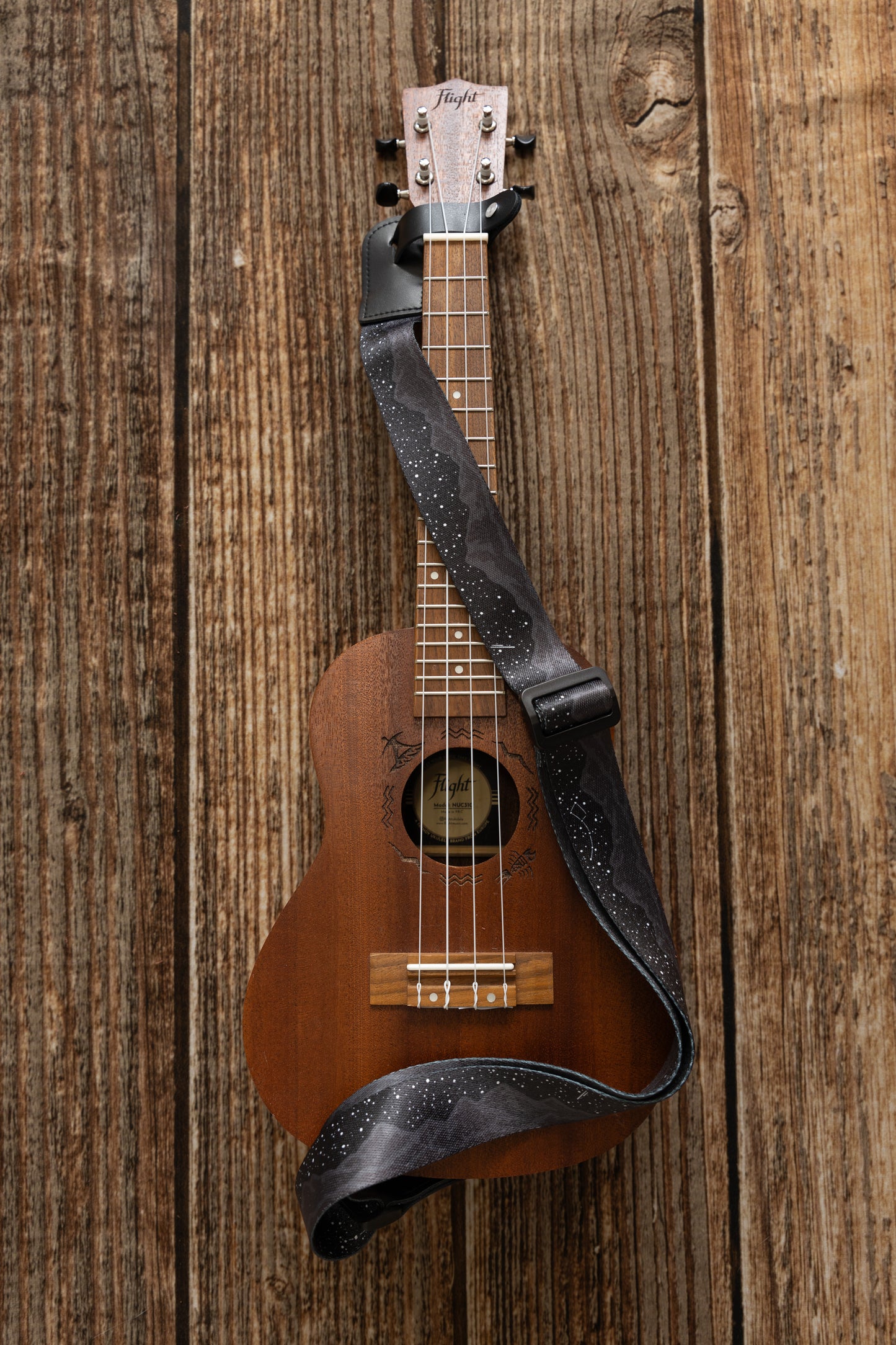 Black Ukulele Strap Strap Printed with Mountains and Stars lying across Ukulele on wood floor