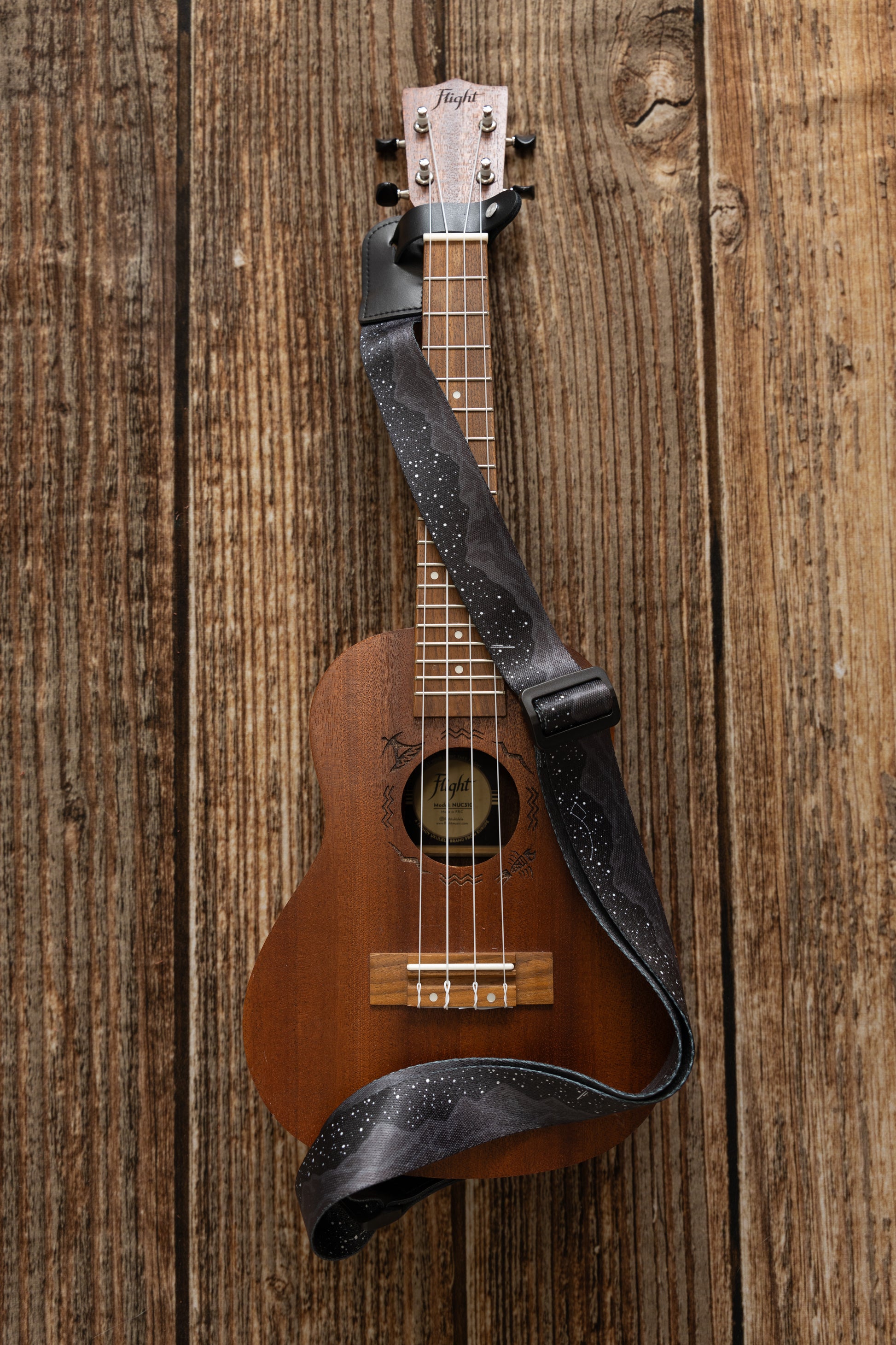 Black Ukulele Strap Strap Printed with Mountains and Stars lying across Ukulele on wood floor