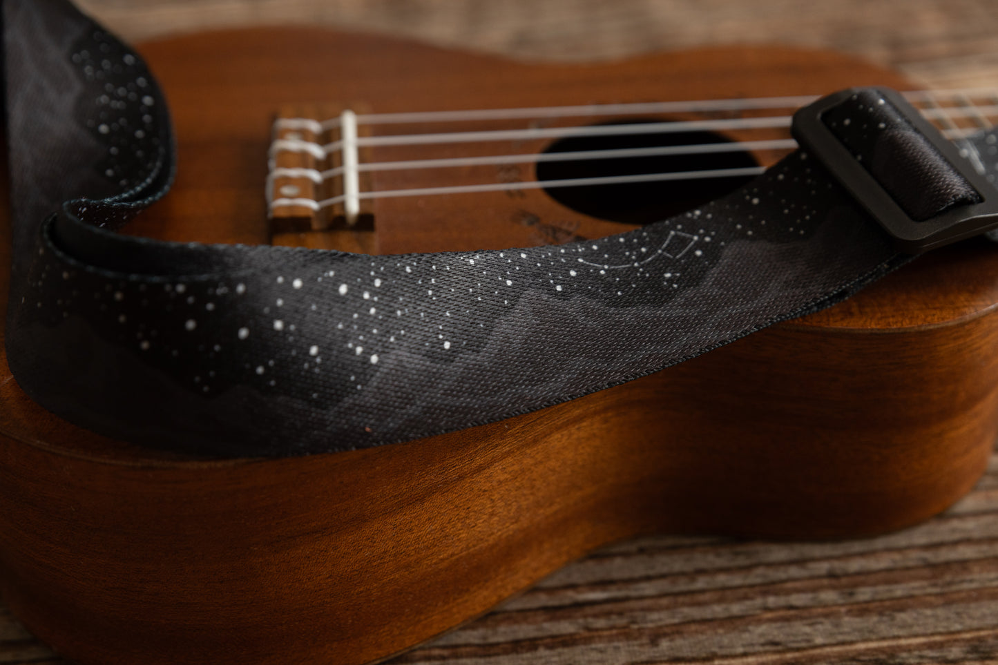 Black Ukulele Strap Strap Printed with Mountains and Stars lying across Ukulele on wood floor