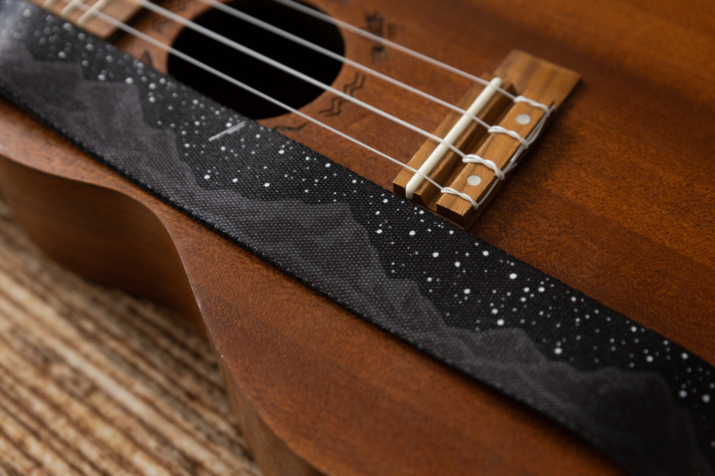 Black Ukulele Strap Strap Printed with Mountains and Stars lying across Ukulele on wood floor