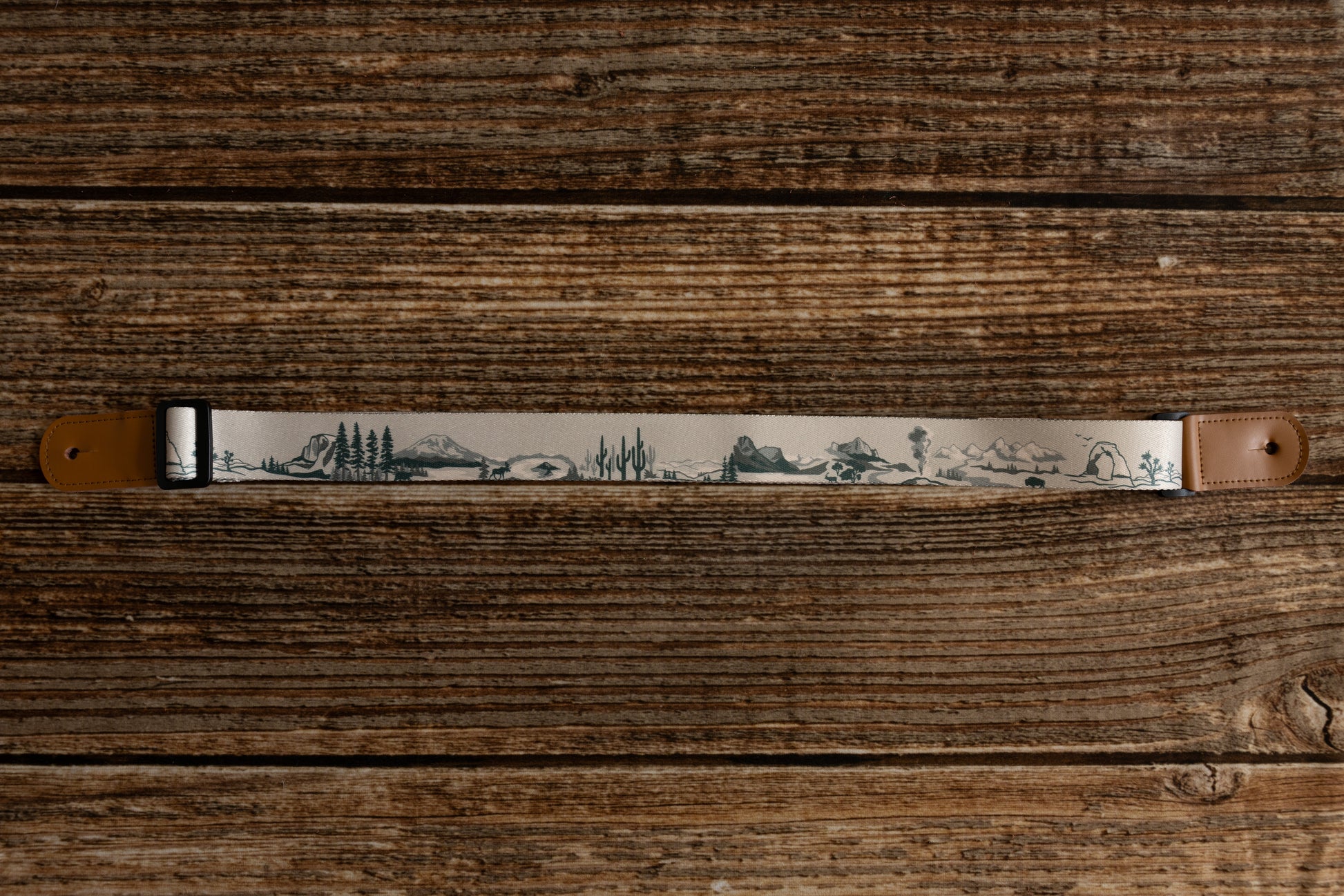 National Park-Themed Ukulele Strap printed with designs of 12 popular national parks along the length of the strap lying on wood floor