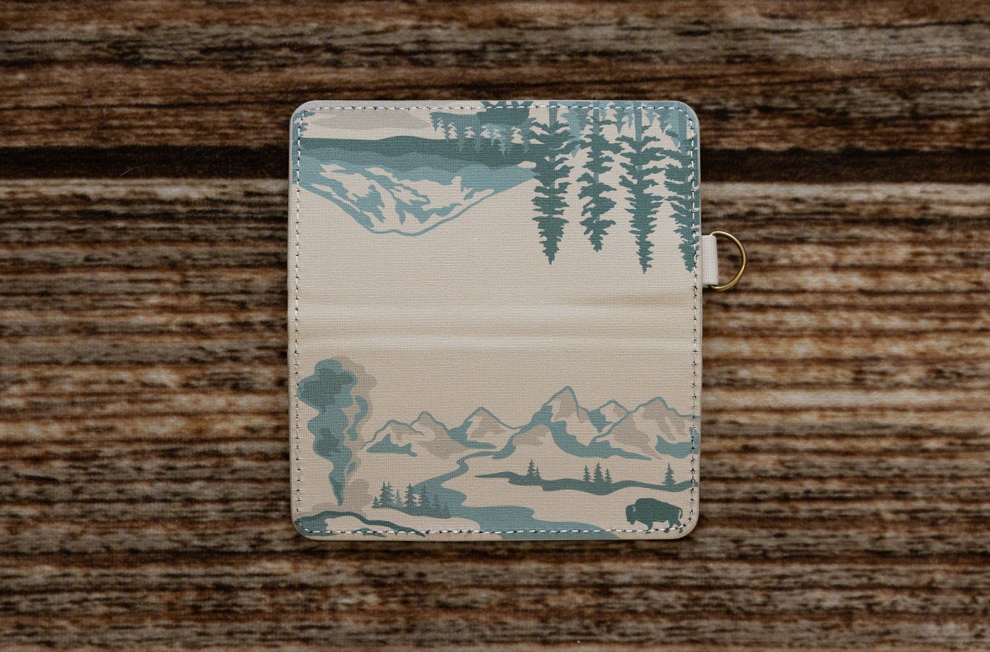 A flat lay of the SD card holder fully unfolded on a wooden surface, displaying a continuous panoramic illustration of a national park landscape with mountains, trees, and a bison.