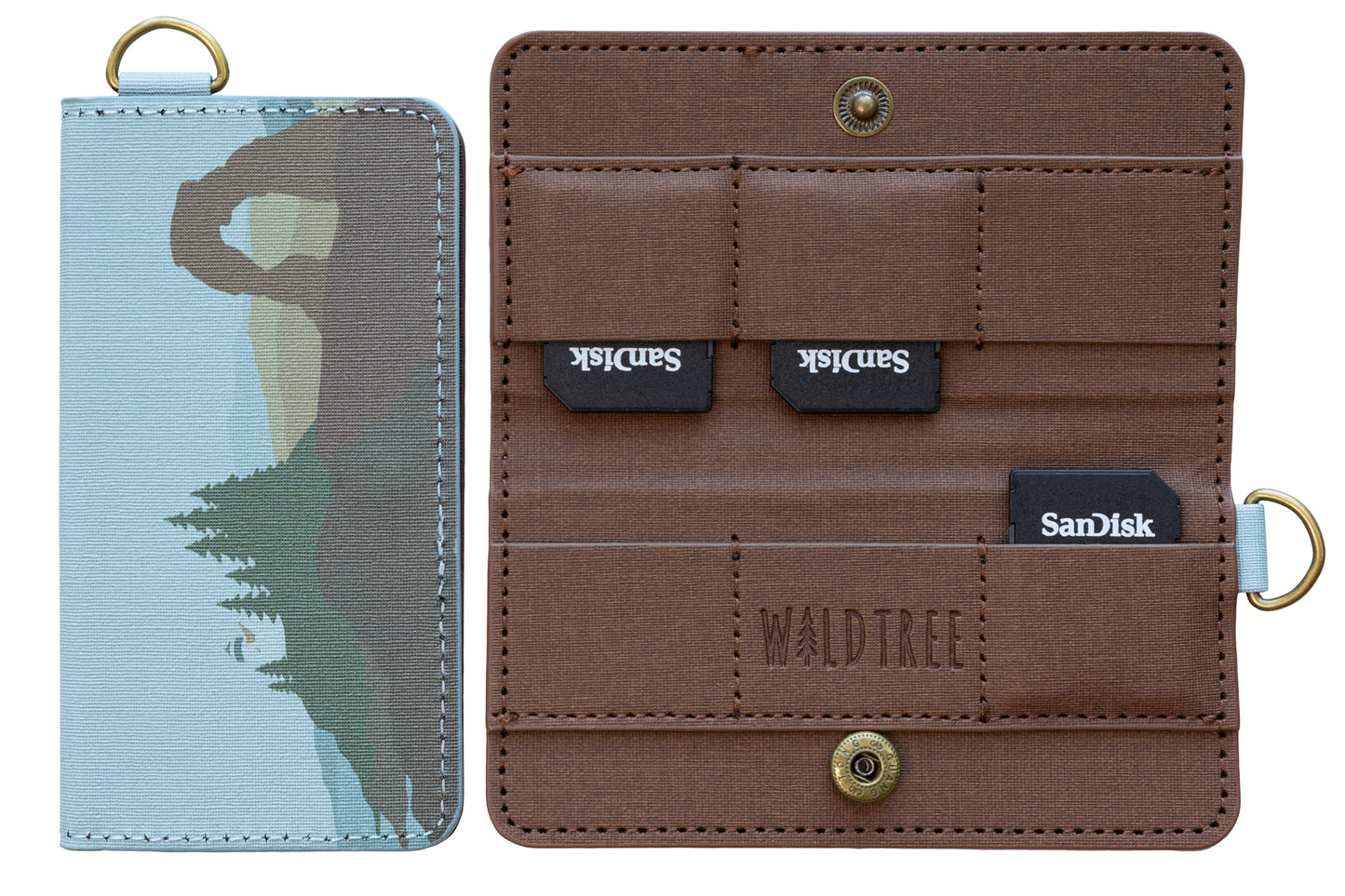 A product isolation shot against a white background showing the Wildtree "Parks in Color" SD card holder. On the left, the closed case displays an artistic graphic of Delicate Arch and pine trees. On the right, the open case shows its brown canvas interior, snap closure, and SanDisk SD cards in its slots.