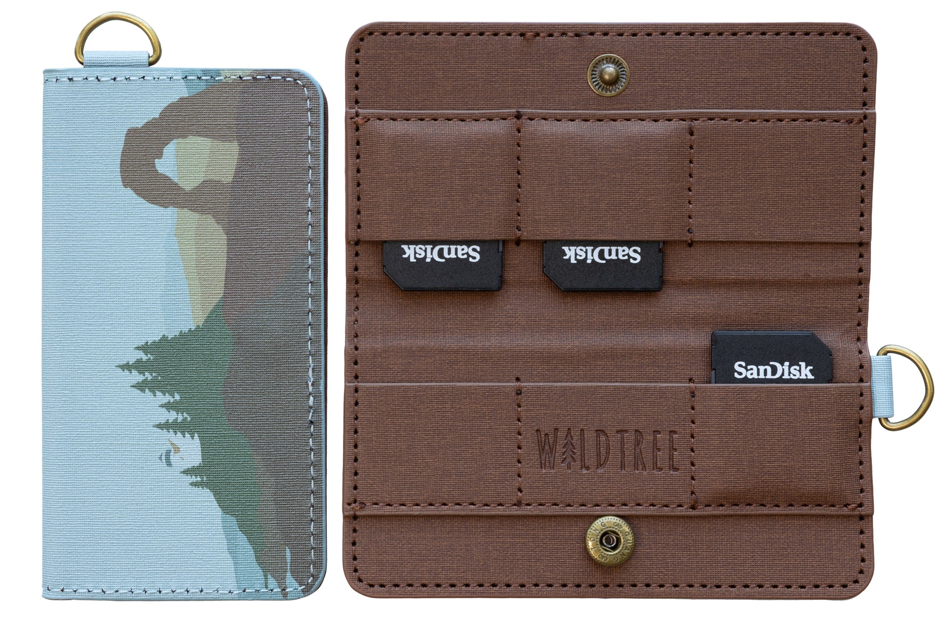 A product isolation shot against a white background showing the Wildtree "Parks in Color" SD card holder. On the left, the closed case displays an artistic graphic of Delicate Arch and pine trees. On the right, the open case shows its brown canvas interior, snap closure, and SanDisk SD cards in its slots.