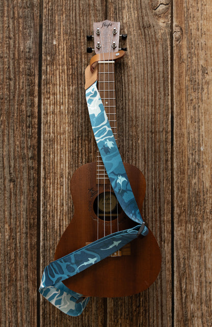 Ocean-designed themed Ukulele Strap. A mix of light and dark blues printed design of ocean water, marine life, turtles, sharks, fish, and manta rays Attached Ukulele lying on wood floor