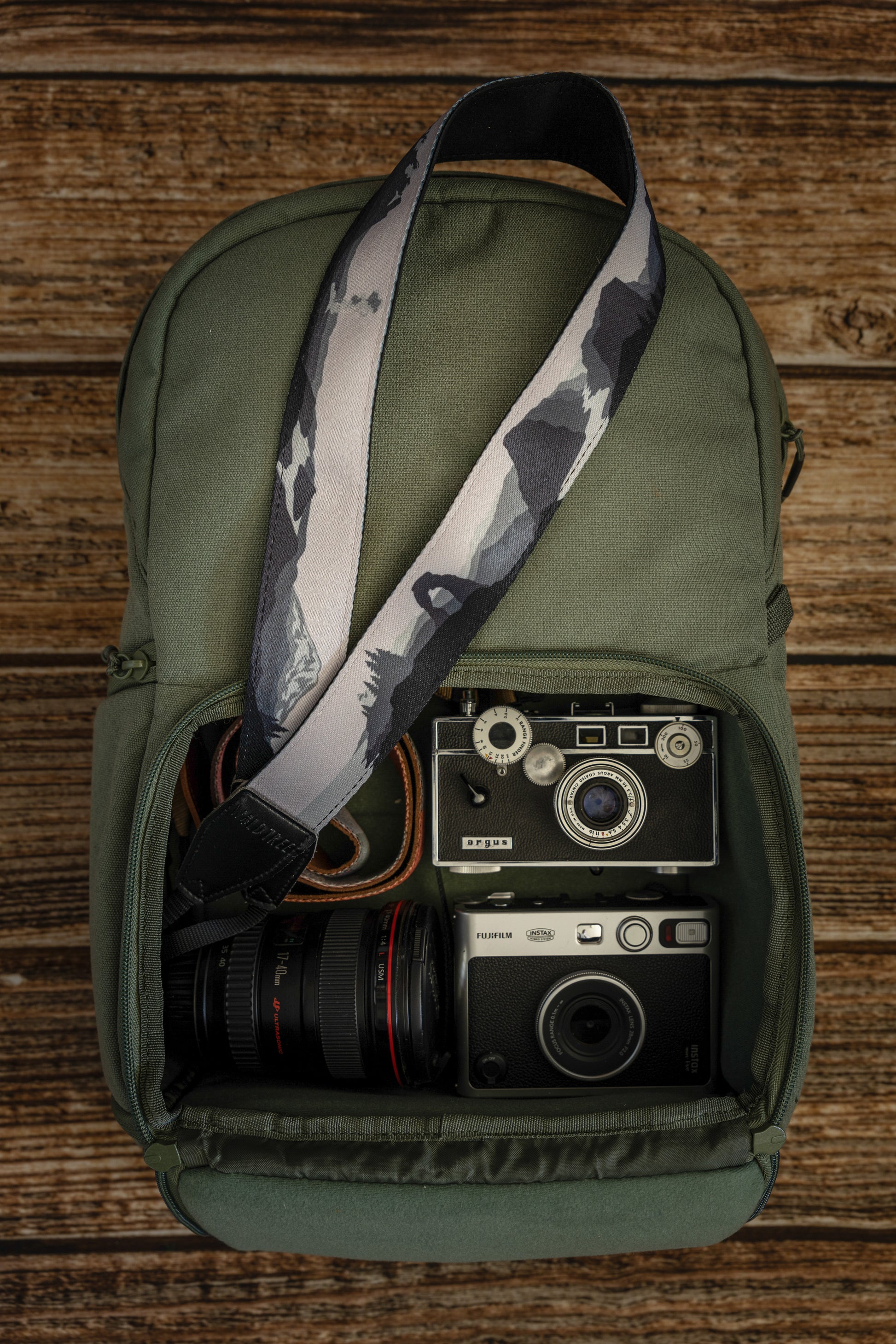 National parks camera strap in black and white laying out on green brevite back pack.