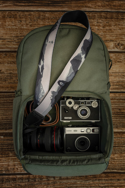 National parks camera strap in black and white laying out on green brevite back pack.