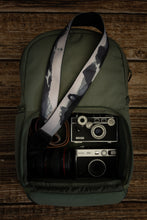 Load image into Gallery viewer, National parks camera strap in black and white laying out on green brevite back pack.
