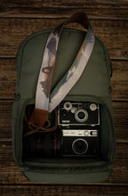 Load image into Gallery viewer, National parks camera strap in color laying out on green brevite back pack. 
