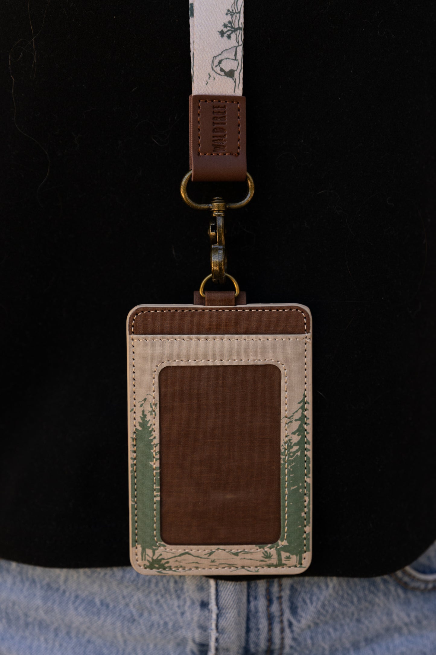 A person outdoors wearing the Yosemite ID badge holder attached to a cream-colored National Parks neck lanyard over a black t-shirt. The lifestyle shot demonstrates exactly where the vertical badge sleeve rests against the chest when worn