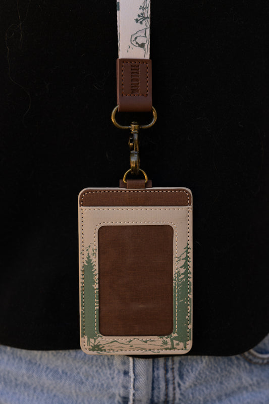 A person outdoors wearing the Yosemite ID badge holder attached to a cream-colored National Parks neck lanyard over a black t-shirt. The lifestyle shot demonstrates exactly where the vertical badge sleeve rests against the chest when worn