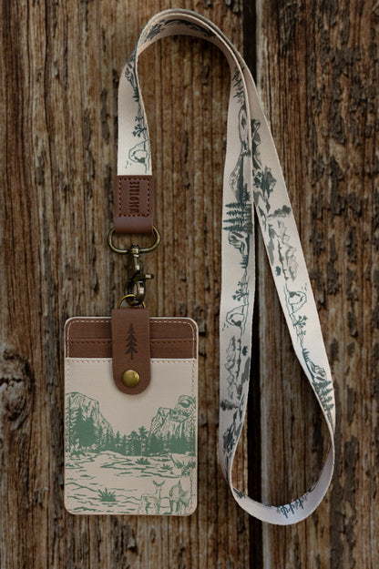A tight close-up shot focusing on the back of the cream Yosemite ID holder attached to a matching lanyard. It showcases the brown vegan leather strap with a stamped tree icon snapped securely over the double card slots.