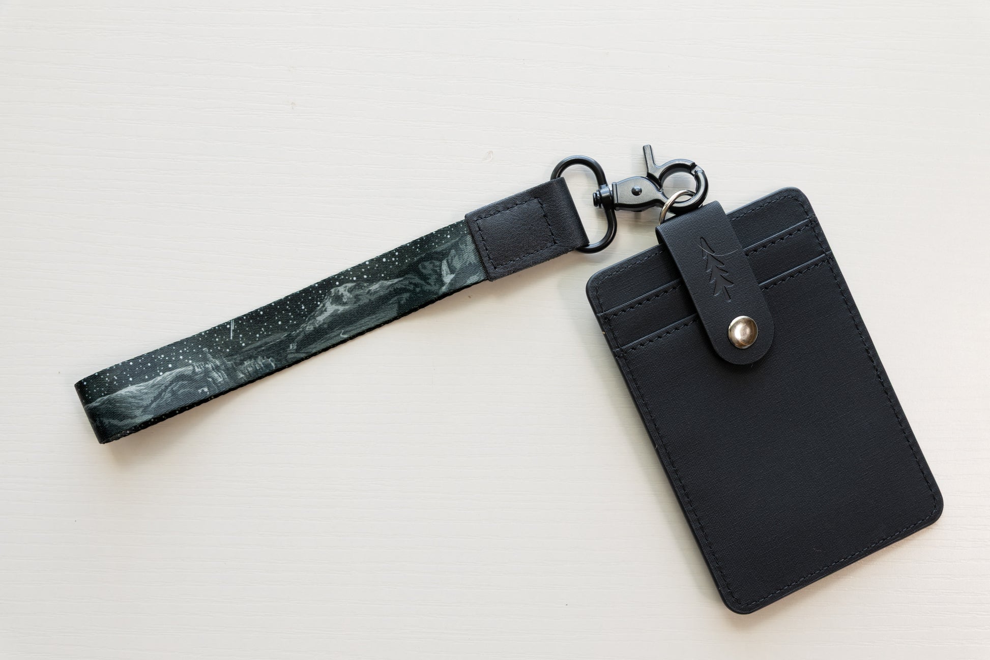 The Parks at Night wristlet keychain attached to an upright black vegan-leather card holder on a white background, showing the black strap printed with mountain silhouettes, scattered stars, and a shooting star.