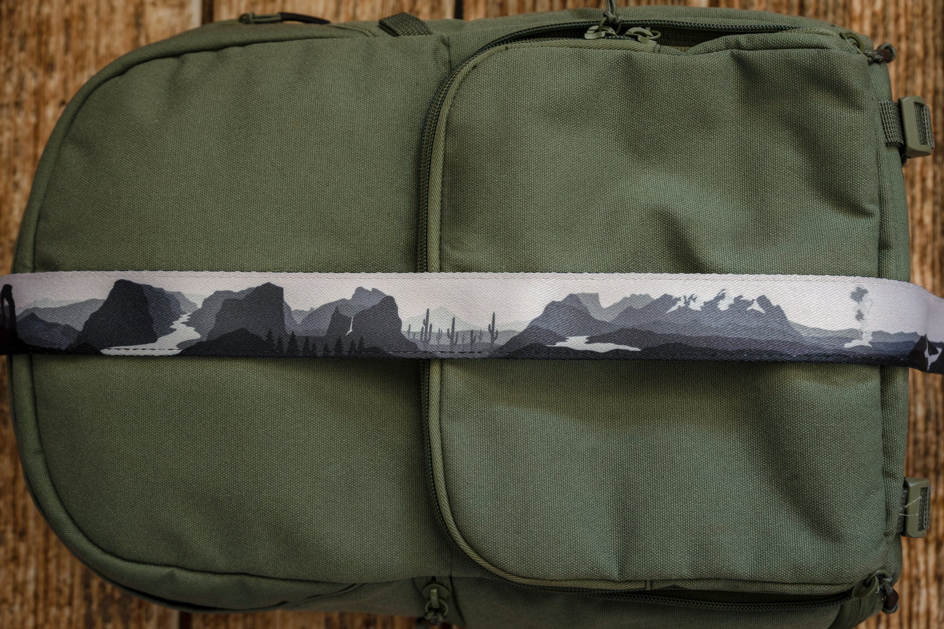 National parks camera strap in black and white laying out on green brevite back pack.