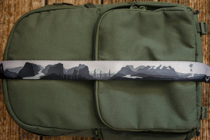 National parks camera strap in black and white laying out on green brevite back pack.