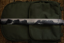 Load image into Gallery viewer, National parks camera strap in black and white laying out on green brevite back pack.

