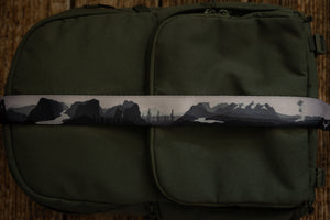 National parks camera strap in black and white laying out on green brevite back pack.