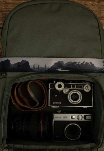 National parks camera strap in black and white laying out on green brevite back pack.