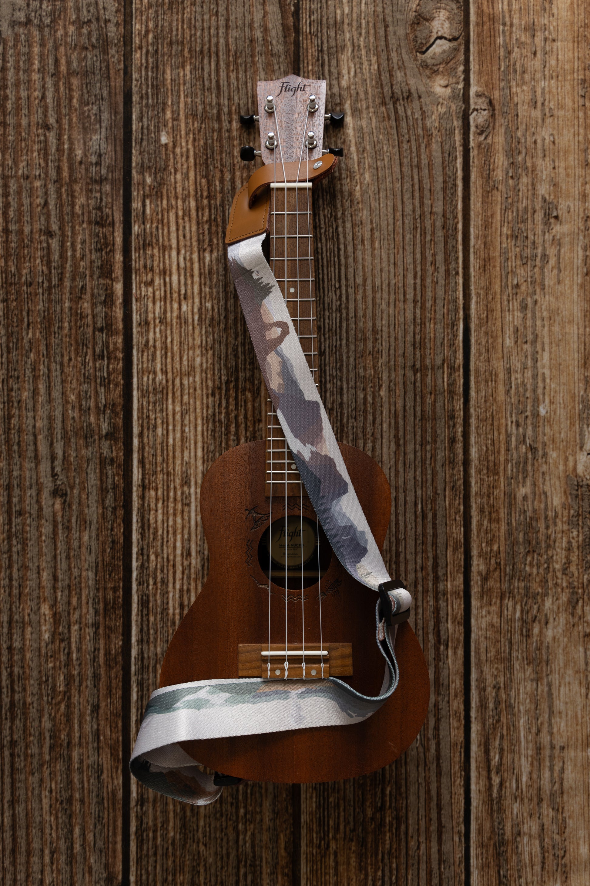 National Park-Themed Ukulele Strap printed with designs of 19 popular national parks along the length of the strap. connected to Ukulele lying on wood floor