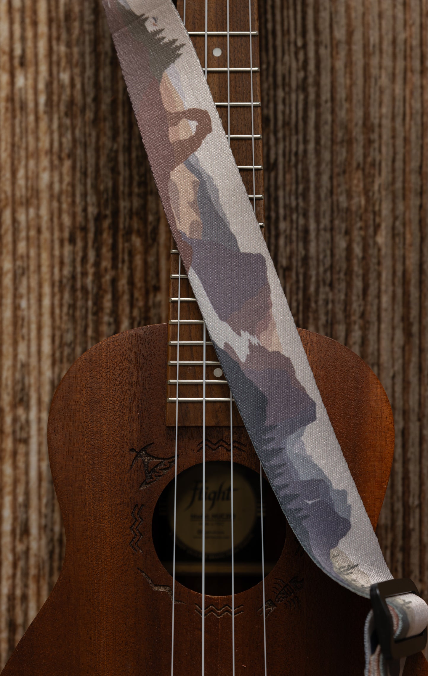 National Park-Themed Ukulele Strap printed with designs of 19 popular national parks along the length of the strap. connected to Ukulele lying on wood floor