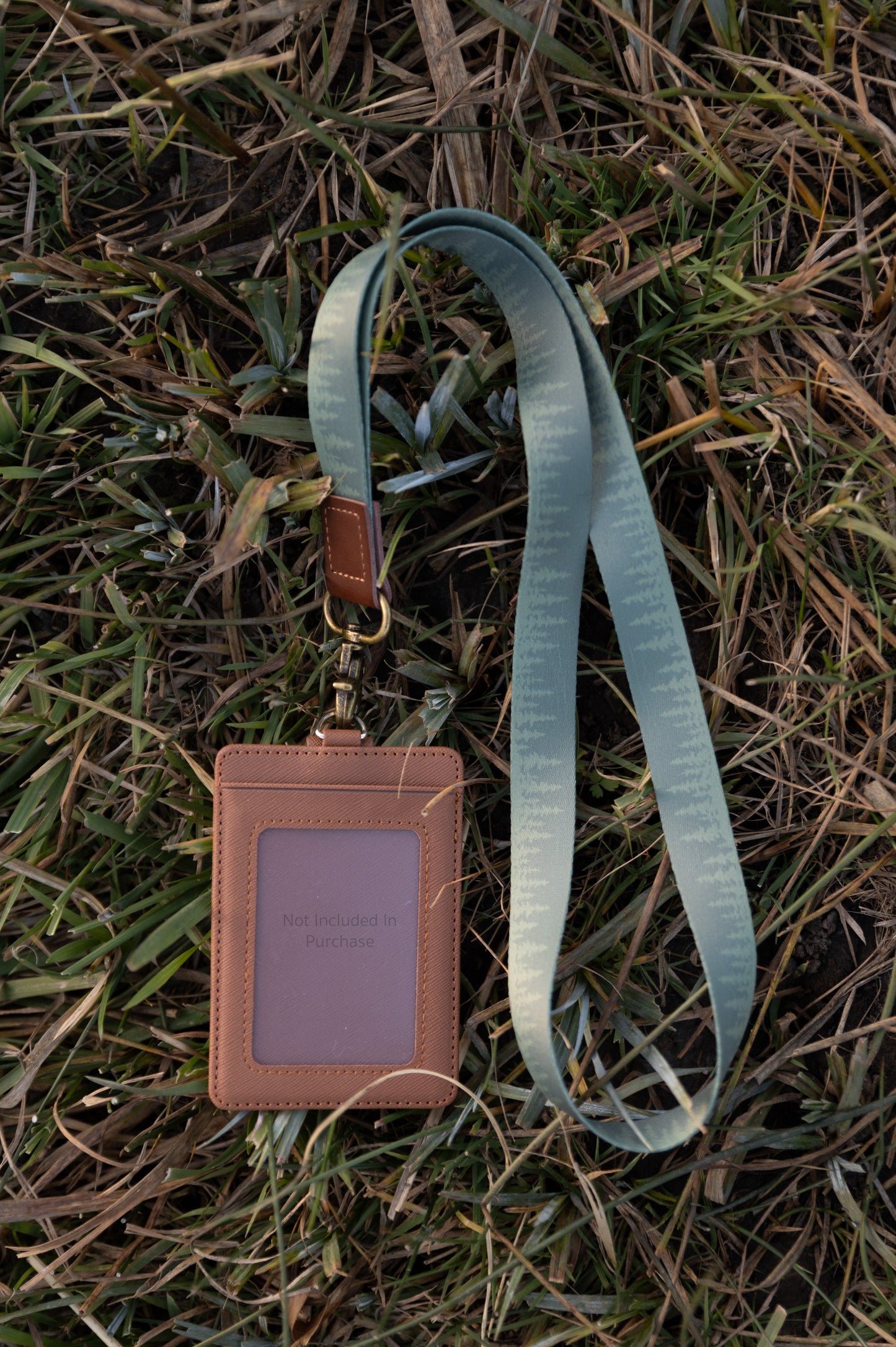 Green Pine tree tree line printed neck lanyard attached to id badge holder lying in grass