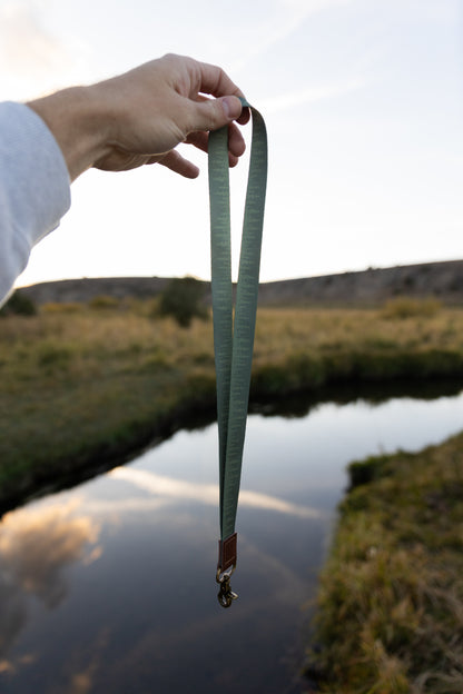 Hand holding out Pinetree printed lanyard in front of river and valley