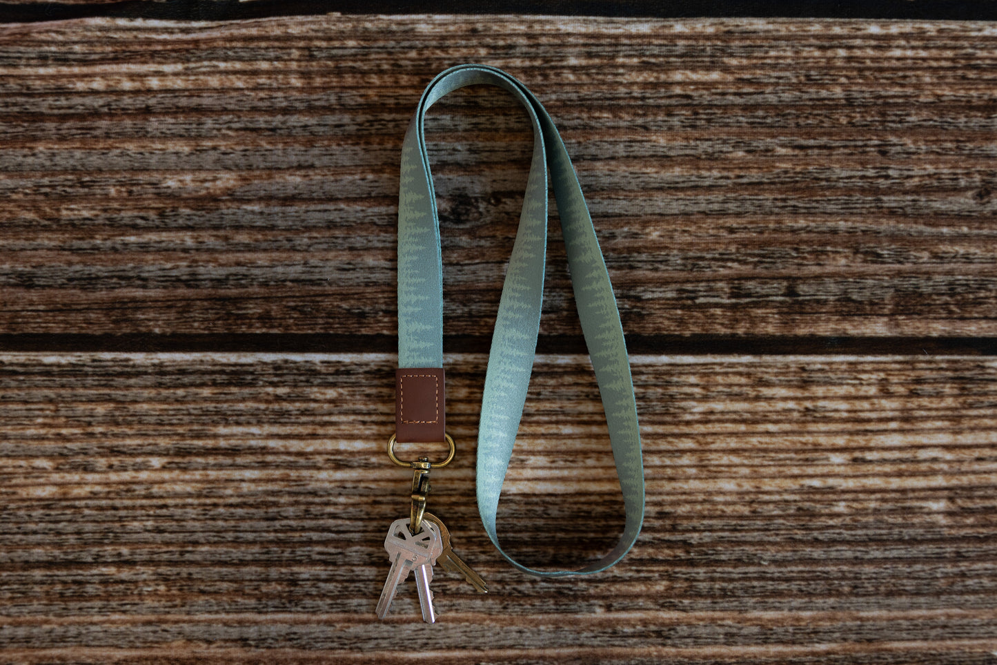 Green Pine tree tree line printed neck lanyard attached to keys lying on wood floor