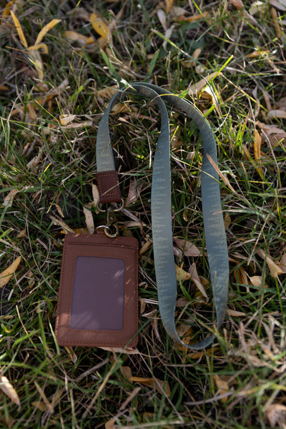 Green Pine tree tree line printed neck lanyard attached to id badge holder lying in grass