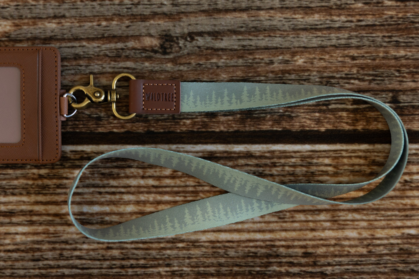 Green Pine tree tree line printed neck lanyard attached to id badge holder lying on wood floor