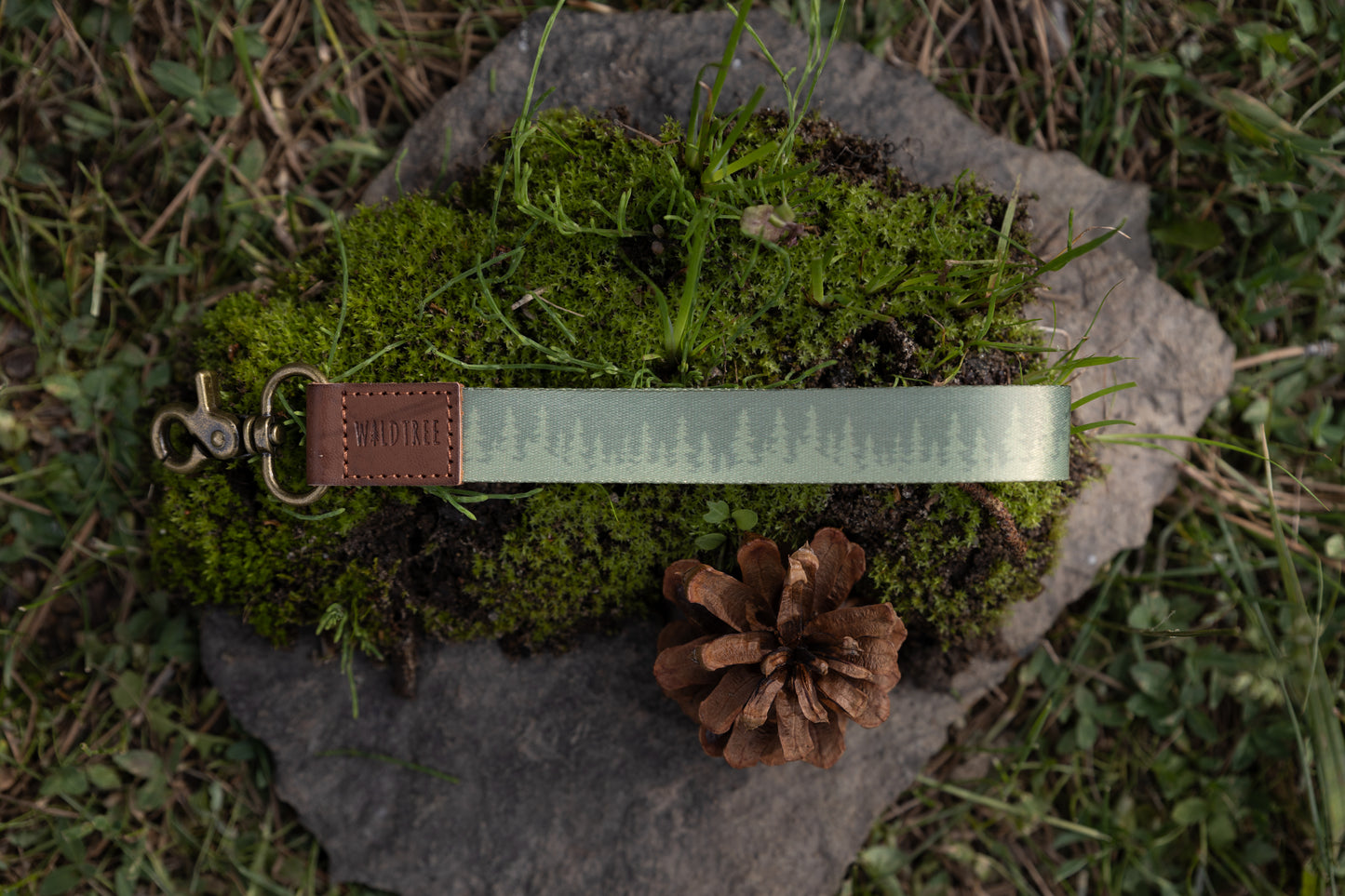Green pinetree wristlet keychain laying on moss and rock