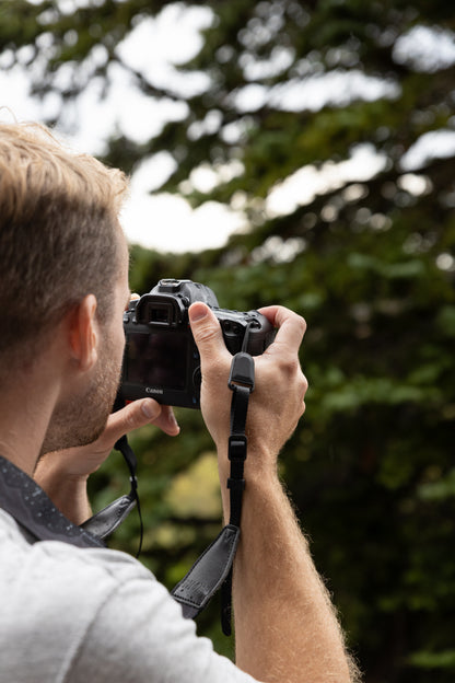 Close-up of a low-profile quick-release buckle connector attached to a tan camera strap and clipped into a camera's split-ring anchor