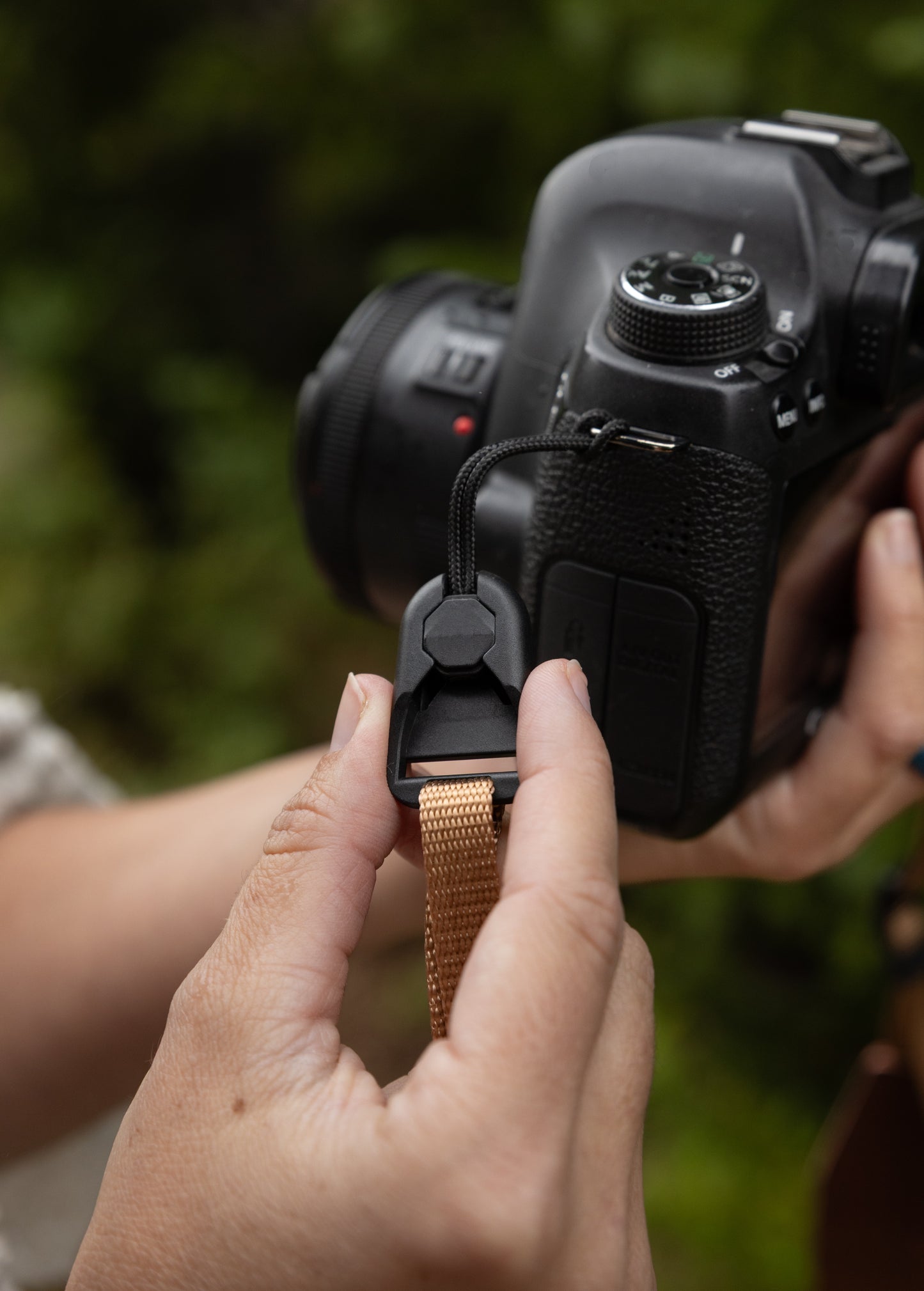 Close-up of hands attaching a tan camera strap to a low-profile quick-release buckle connector secured to the camera body